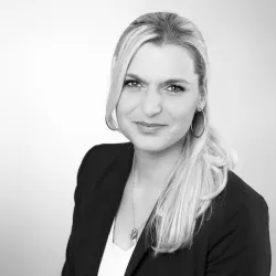 Blonde Frau mit offenen Haaren lächelt in dunklem Blazer